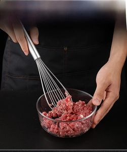 Action shot of a stainless steel whisk mixing meat in a glass bowl for kitchen cooking