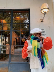 Close-up of a colorful rainbow plaid scarf with tassels worn by a model in a cafe setting