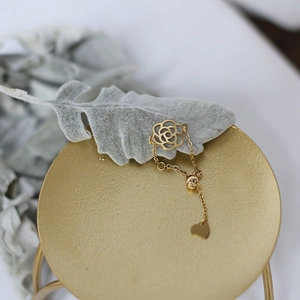 Macro shot of 14K gold camellia ring with heart pendant and adjustable chain detail