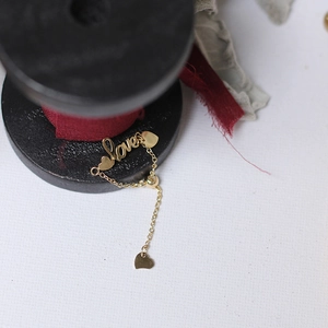 Detail of adjustable gold-plated chain bracelet featuring Love lettering and heart charms