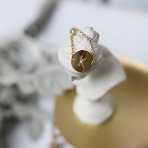 Macro detail of 14K gold-plated chain ring featuring a hollow K-letter pendant on a statue