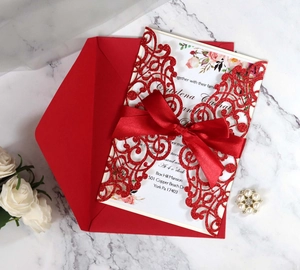 Close-up of laser-cut red wedding invitation with satin bow and white printed insert