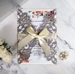 Macro detail of laser-cut silver glitter wedding invitation with an ivory satin bow