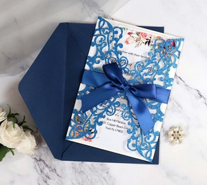 Flat lay of laser-cut glitter blue wedding invitation set with ribbon and floral insert