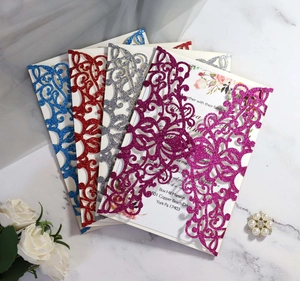 Laser-cut glitter wedding invitations in blue, red, silver and rose on marble surface