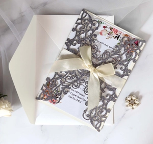 Detail of silver glitter laser-cut wedding invitation with beige ribbon and matching envelope
