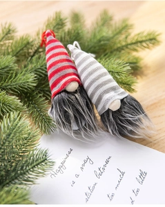 Detail of Christmas gnomes ornaments with striped hats and pine branches on wooden table