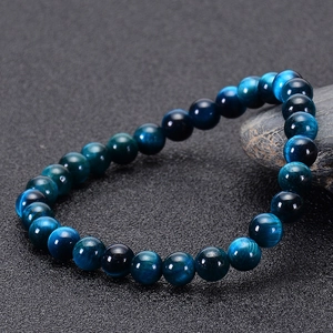 Macro shot of blue tiger eye stone beads on a textured surface showing chatoyancy effect