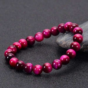 Macro shot of rose red tiger eye stone beads bracelet with cat-eye effect on black background
