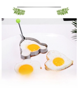 Bear-shaped stainless steel egg mold with a green heat-resistant handle and fried eggs
