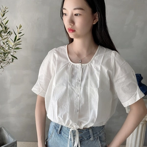 Detail of short sleeve white cotton blouse with pleated neckline and drawstring hem