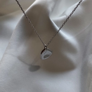 Detailed close-up of a minimalist silver pendant necklace on white silk fabric background