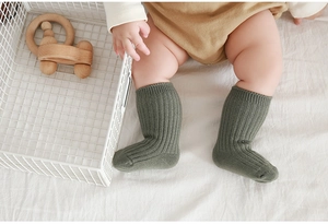 Close-up of military green ribbed cotton baby socks worn by an infant on a white bed