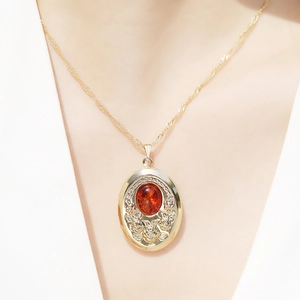 Collana vintage dorata con ciondolo ovale a medaglione, gemma rosso ambra e rilievo floreale