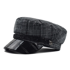 Detail of checkered newsboy cap with crocodile pattern leather brim and metal buttons