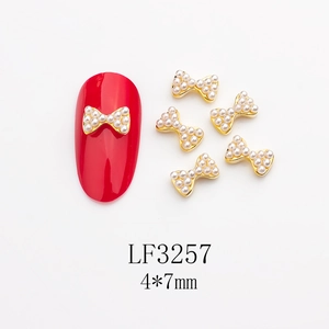 Détail de bijoux d'ongles nœuds dorés 4x7mm avec perles sur présentoir rouge