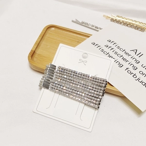 Eight silver rhinestone bobby pins displayed on a card over a decorative wooden tray