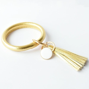 Detail of a gold faux leather ring keychain with long fringe tassel and white pendant tag