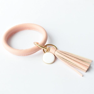Close-up of pink leather bangle keychain with tassel, gold hardware and round charm