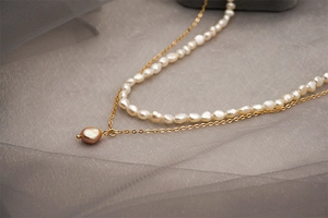 Détail d'un collier double rang en perles d'eau douce baroques avec chaîne dorée et pendentif