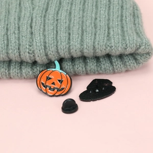 Halloween pumpkin enamel brooch set against pink background with a cozy gray knit hat