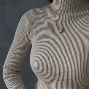 Close-up of a minimalist 925 silver square pendant necklace worn over a beige sweater