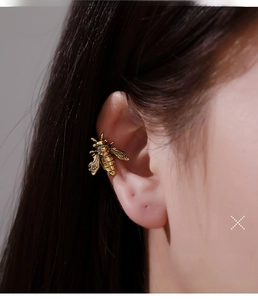 Macro view of vintage gold bee ear cuff with detailed metal texture on a model's ear