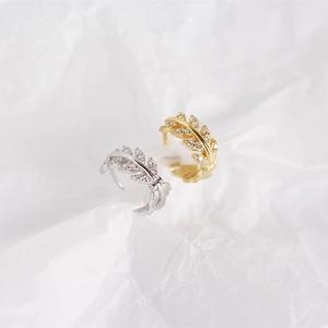 Detailed view of silver and gold olive leaf rings with sparkling zircon on white paper