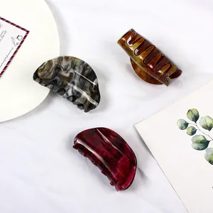 Detail of large marble and amber patterns acetate hair claws on a clean white fabric background