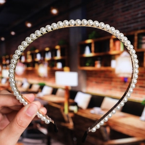 Detail of white pearls on golden metal headband with black protective end tips