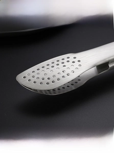 Détail d'une pince de cuisine en acier inoxydable avec verrouillage et trous de drainage