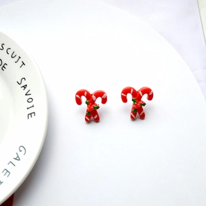 Detailed close-up of red and white candy cane Christmas earrings with green leaf accent