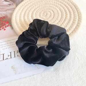 Detail of a soft black velvet scrunchie placed on a textured straw mat with lifestyle props