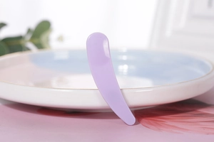 Macro shot of a purple curved cosmetic spatula on a ceramic dish for facial cream use