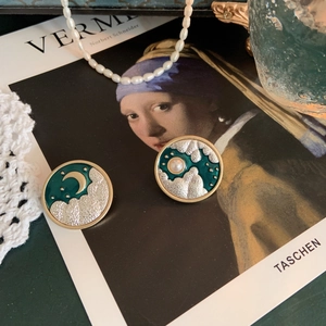 Detailed macro of vintage moon and sun asymmetric earrings with green enamel coating