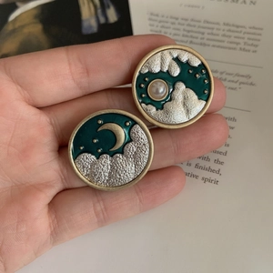 Macro view of vintage round sun and moon enamel earrings with pearl detail held in hand