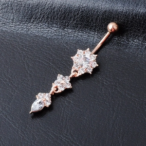 Rose gold belly ring with flower and teardrop pendants on black leather surface