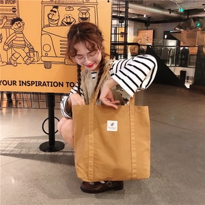 Khaki canvas tote bag shown with shoulder strap details and a white fabric patch label