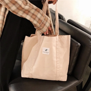 Detail of beige canvas tote bag showing textile patch and natural cotton texture
