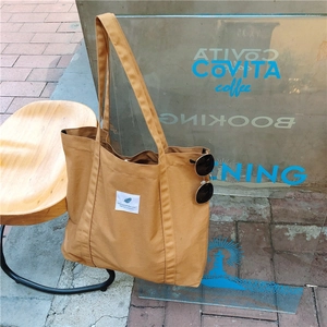 Detail of caramel canvas tote bag placed on a wooden stool with sunglasses accessory