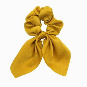 Bright yellow satin scrunchie with long ribbon bow tie hair accessory on white background