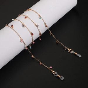 Golden metal eyewear chain with colorful evil eye charms on a minimal white pedestal