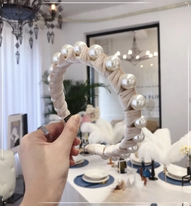 Detail of elegant beige velvet headband with large white pearls held by hand in a room
