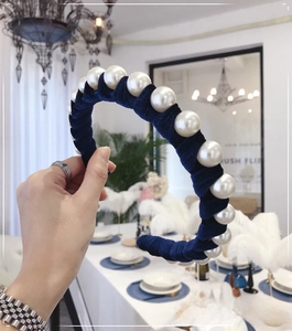 Detail of dark blue velvet headband with large white pearls shown in a hand-held view
