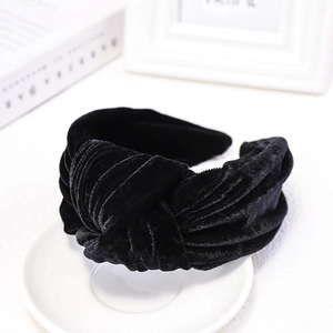 Detail view of a black velvet knotted headband on a white ceramic plate backdrop