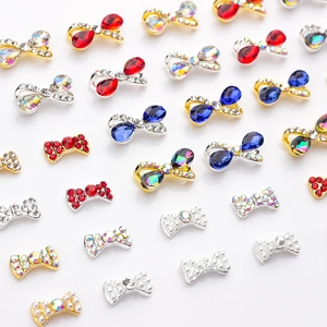 Assortimento di fiocchi in lega per nail art con strass colorati su sfondo bianco