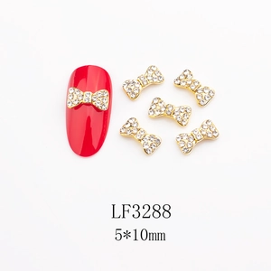 Dettaglio macro di ciondoli per unghie a fiocco dorati 5x10mm con strass su unghie rosse