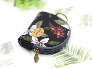 Detail of a floral print cotton coin purse with a brown leather label and bronze zipper