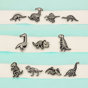 Set of 11 white enamel dinosaur fossil pins on textured cotton straps