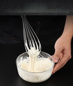 Macro detail of stainless steel whisk mixing thick white batter in a glass bowl